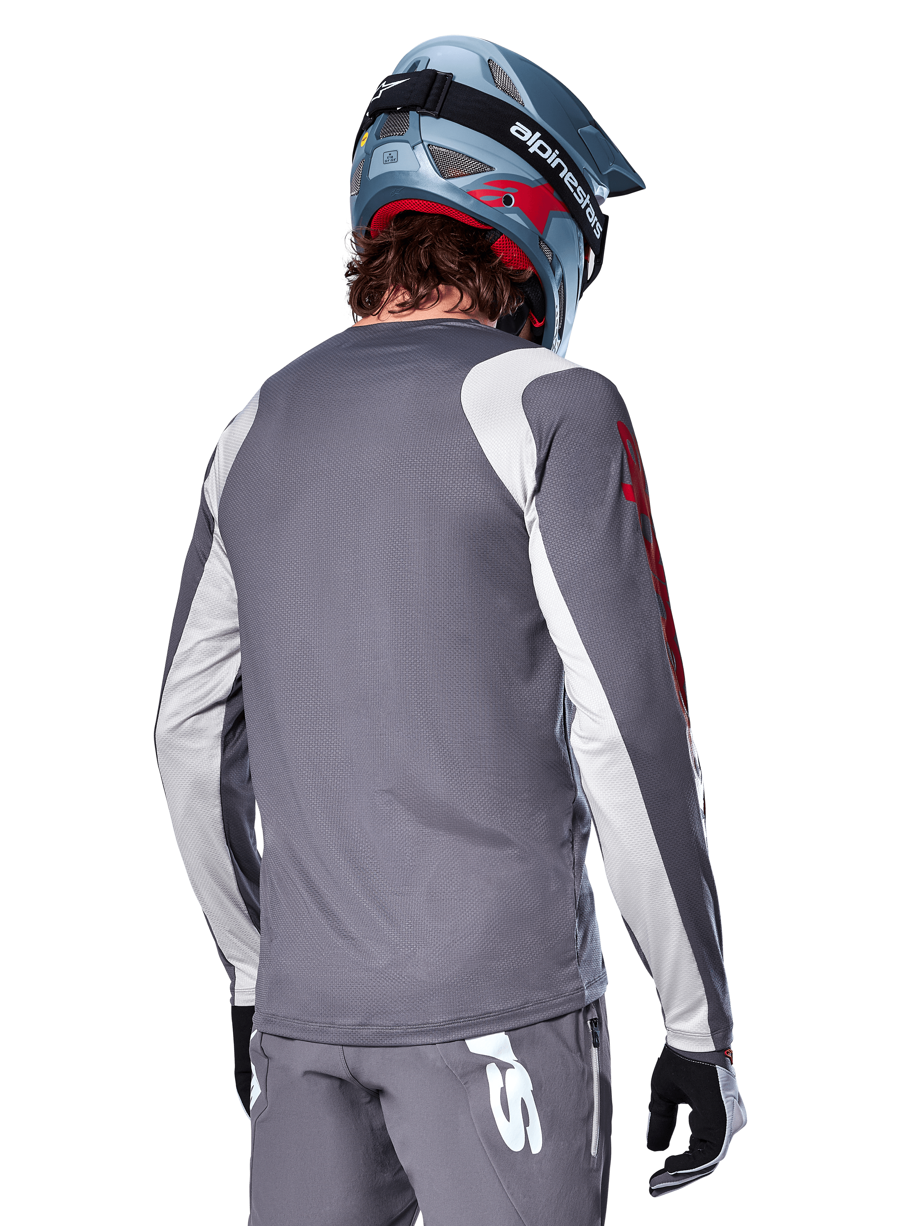 Jersey Alpinestars A-Supra Astar de manga larga, gris oscuro con paneles en gris claro en hombros y brazos, vista trasera del ciclista con casco integral de MTB azul y pantalones grises, ropa de ciclismo MTB de alto rendimiento