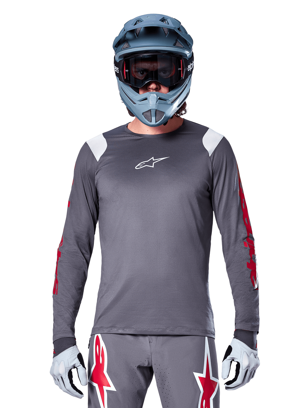 Ciclista de MTB con jersey de manga larga Alpinestars A-Supra Astar, gris oscuro con gráficos rojos en las mangas y detalles blancos en los hombros, pantalones grises a juego con logotipos de estrellas rojas, casco integral azul y gafas, equipamiento coordinado para ciclismo todoterreno