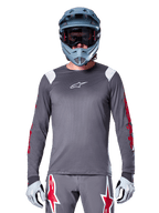 Ciclista de MTB con jersey de manga larga Alpinestars A-Supra Astar, gris oscuro con gráficos rojos en las mangas y detalles blancos en los hombros, pantalones grises a juego con logotipos de estrellas rojas, casco integral azul y gafas, equipamiento coordinado para ciclismo todoterreno
