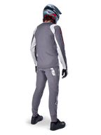 Alpinestars Jersey A-Supra Astar, jersey de MTB de manga larga, gris oscuro con detalles blancos en las mangas y logotipo rojo, vista trasera del ciclista con pantalones grises a juego y casco integral azul, ropa de ciclismo de alto rendimiento