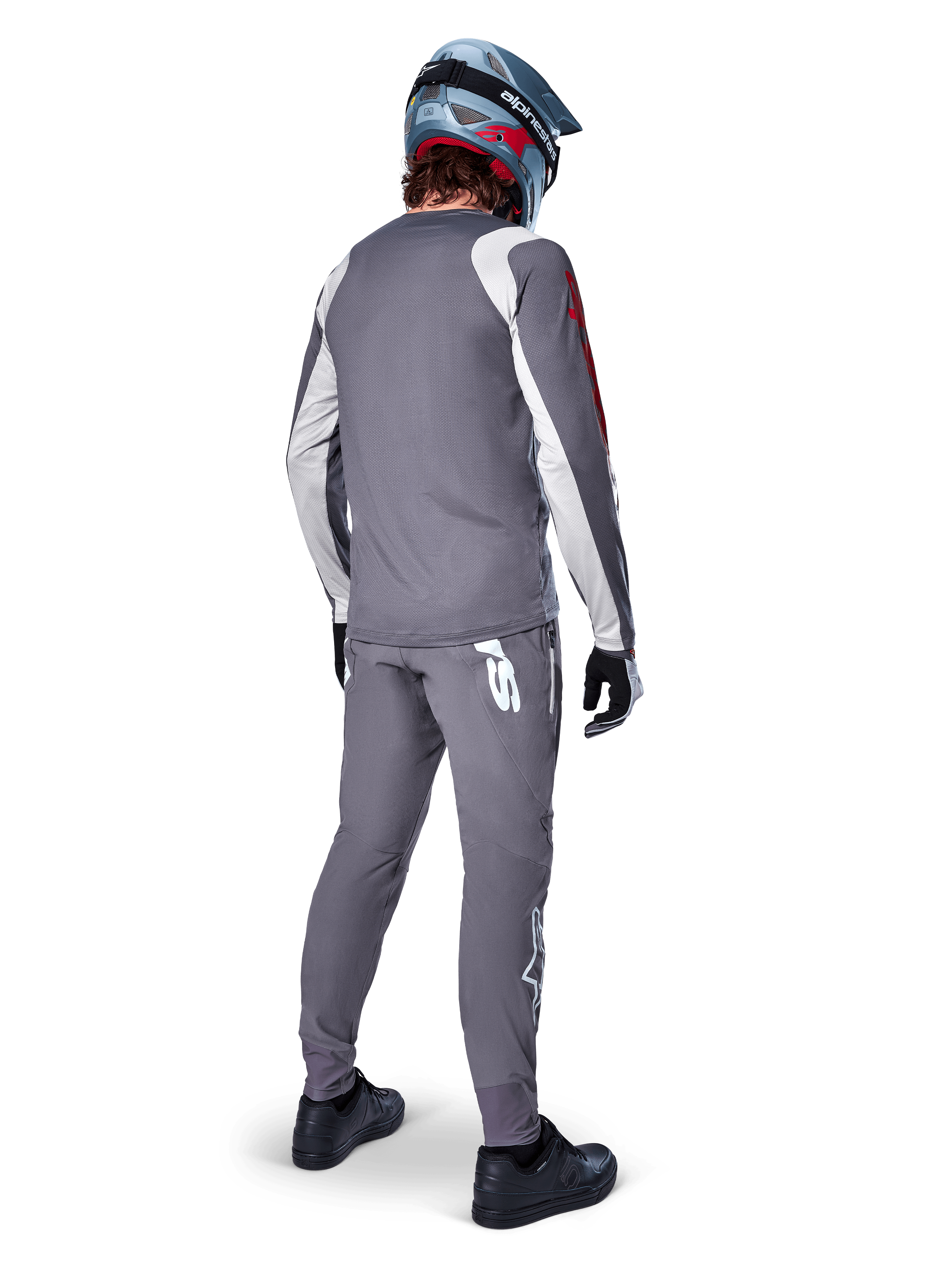 Alpinestars Jersey A-Supra Astar, jersey de MTB de manga larga, gris oscuro con detalles blancos en las mangas y logotipo rojo, vista trasera del ciclista con pantalones grises a juego y casco integral azul, ropa de ciclismo de alto rendimiento