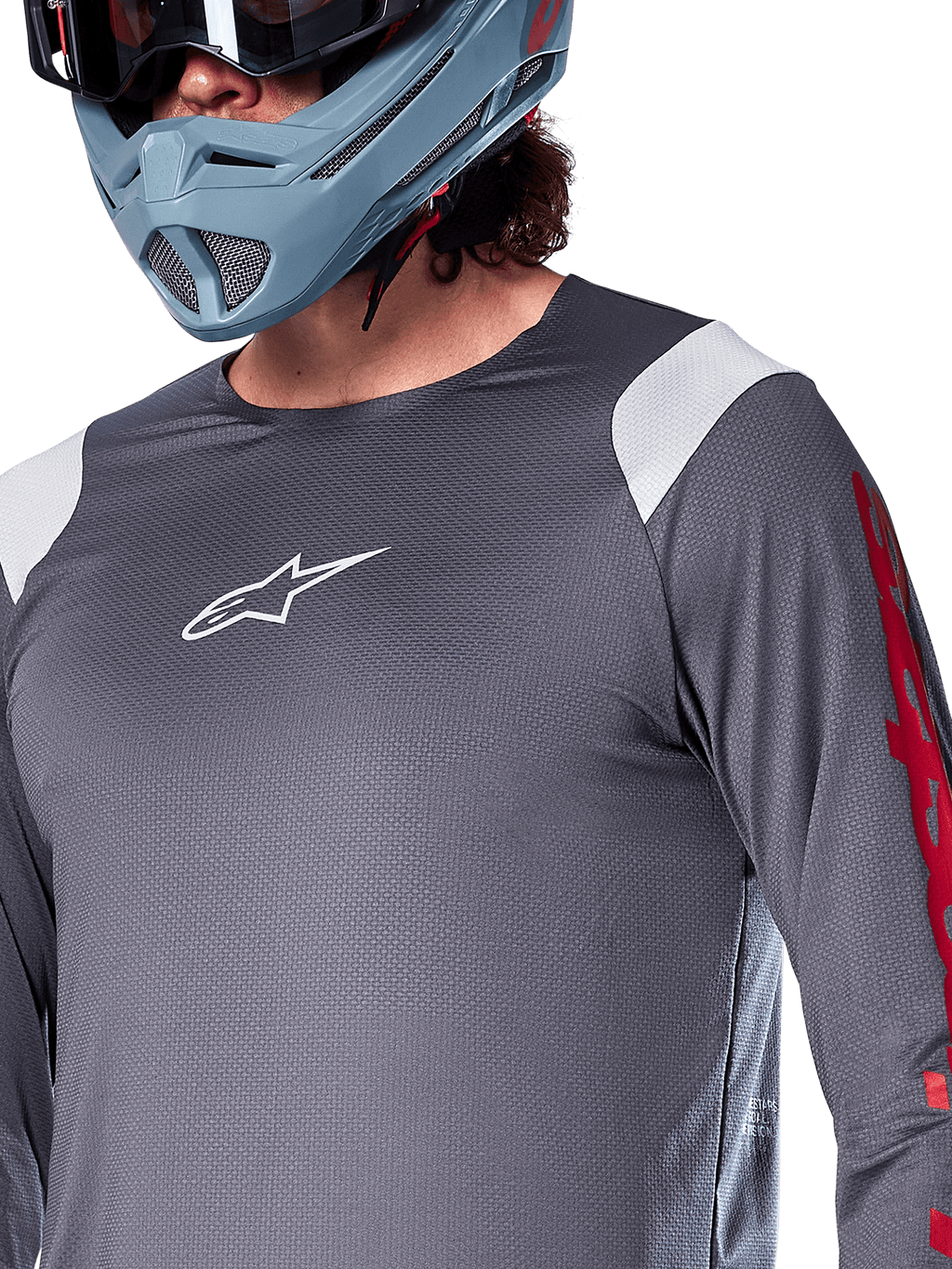 Jersey de manga larga Alpinestars A-Supra Astar, gris oscuro con paneles blancos en los hombros y gráficos rojos en las mangas, usado con un casco integral gris azulado claro, equipamiento de alto rendimiento para bicicleta de montaña