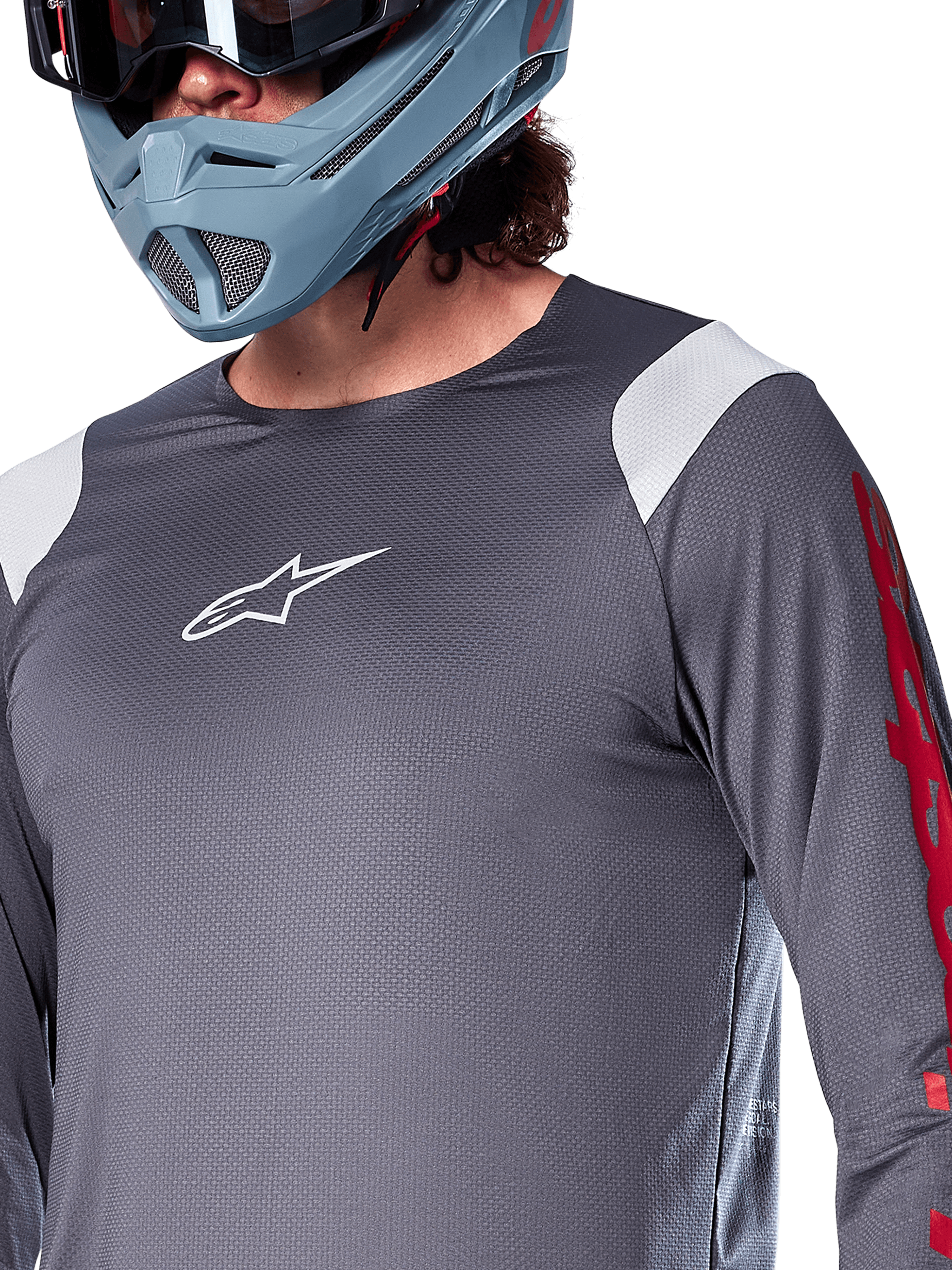 Jersey de manga larga Alpinestars A-Supra Astar, gris oscuro con paneles blancos en los hombros y gráficos rojos en las mangas, usado con un casco integral gris azulado claro, equipamiento de alto rendimiento para bicicleta de montaña