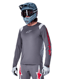 Alpinestars A-Supra Astar Jersey de manga larga, jersey para ciclismo de montaña MTB, gris oscuro con detalles rojos y blancos, ajuste de rendimiento, usado con pantalones grises a juego con gráficos de estrellas rojas y blancas, equipo completo de ciclismo todoterreno con casco integral y guantes