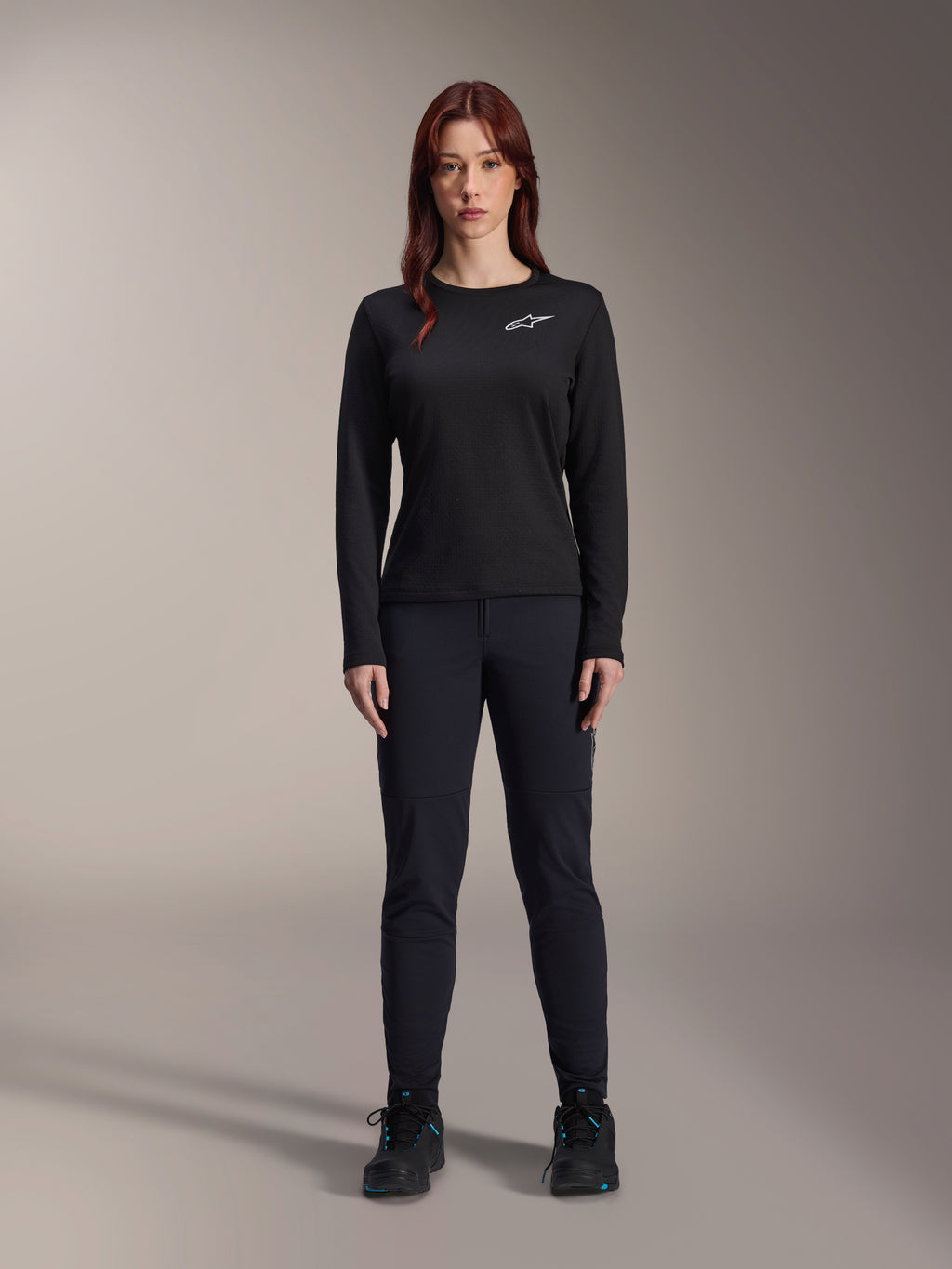 Alpinestars Stella A-Dura Thermal Jersey, jersey de ciclismo de montaña de manga larga para mujer en color negro, con un logotipo blanco en el pecho, combinado con equipamiento negro a juego y zapatillas de ciclismo, retrato de estudio.