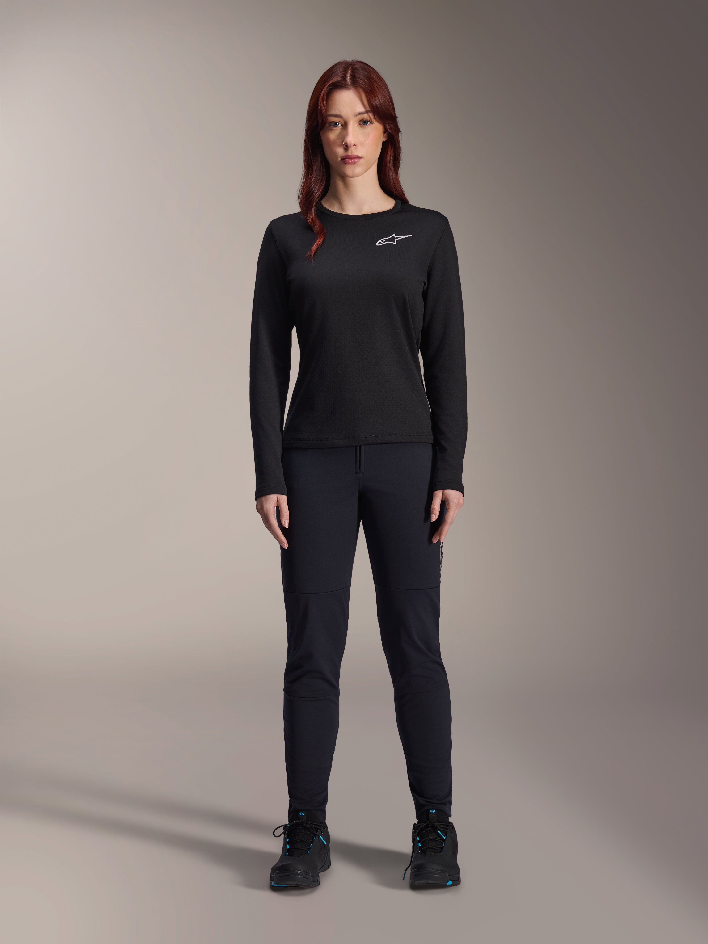 Alpinestars Stella A-Dura Thermal Jersey, jersey de ciclismo de montaña de manga larga para mujer en color negro, con un logotipo blanco en el pecho, combinado con equipamiento negro a juego y zapatillas de ciclismo, retrato de estudio.