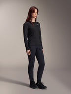 Mujer vistiendo el Jersey Térmico Alpinestars Stella A-Dura, jersey de MTB de manga larga en color negro con logotipo blanco en el pecho, combinado con pantalones negros a juego y calzado deportivo, retrato de estudio de ropa de ciclismo de alto rendimiento