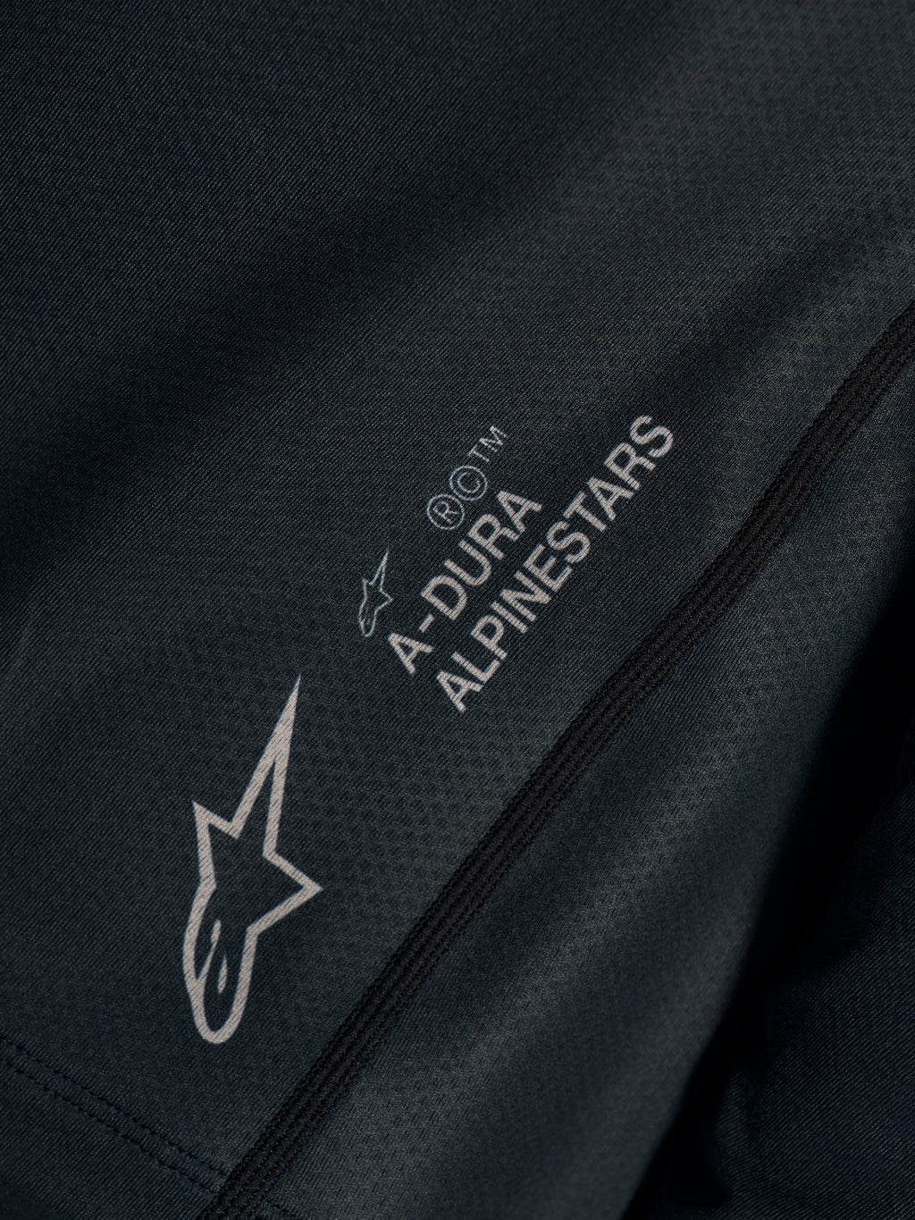 Primer plano del jersey Stella A-Dura Ride negro en tejido jacquard técnico con logotipos A-Dura Alpinestars y Astars.
