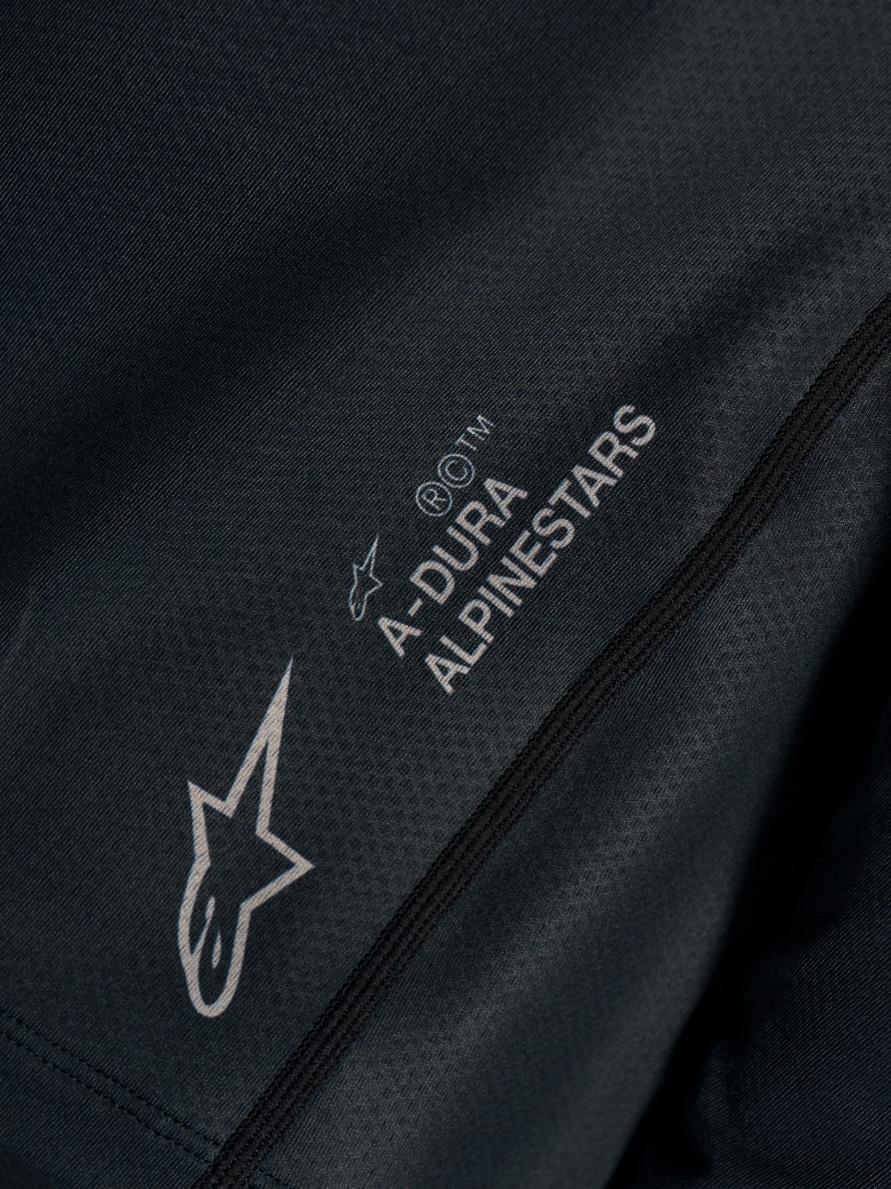 Primer plano del jersey Stella A-Dura Ride negro en tejido jacquard técnico con logotipos A-Dura Alpinestars y Astars.