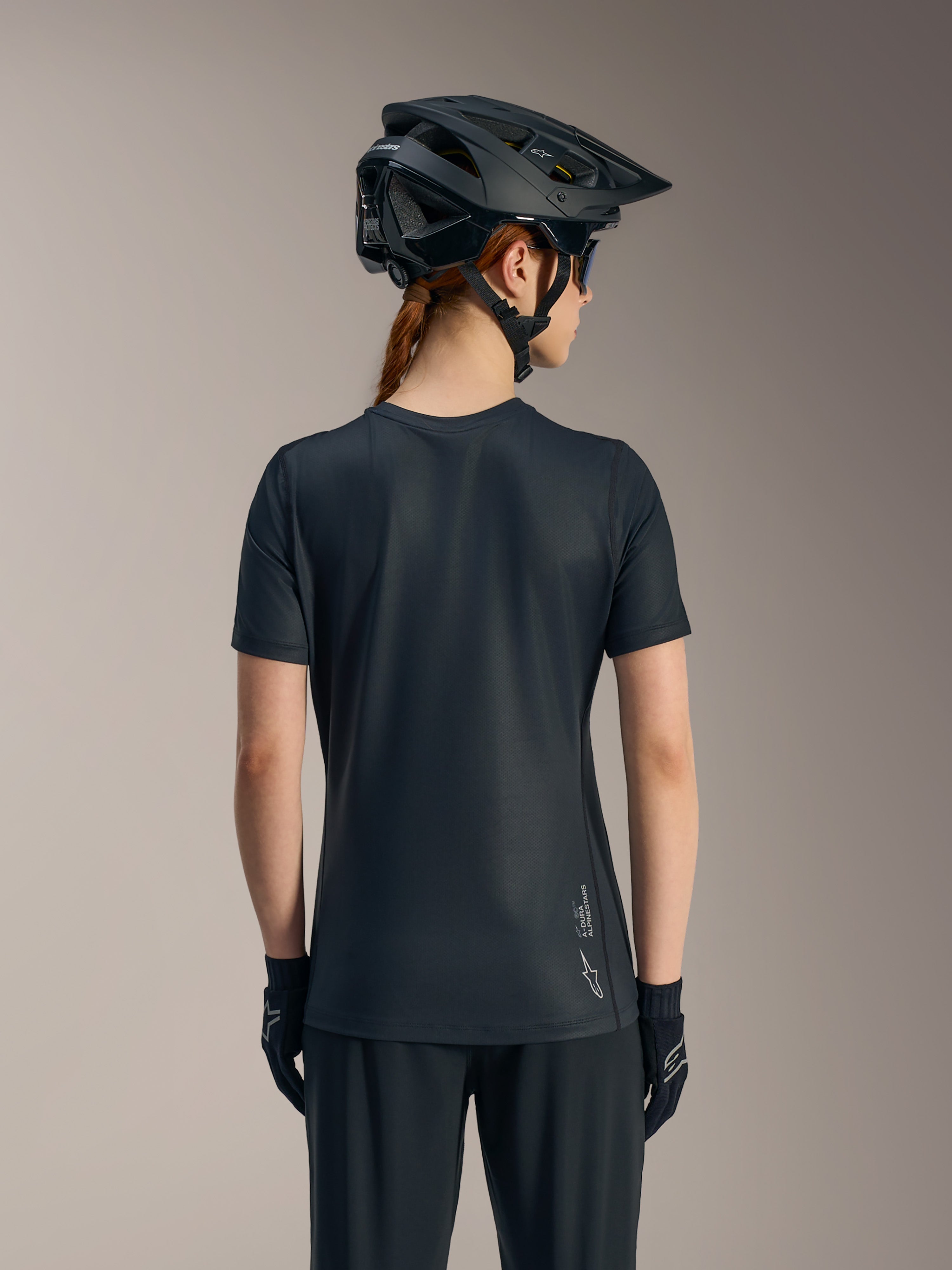 Jersey negro Stella A-Dura Ride de manga corta para mujer, vista trasera con cola caída y logotipo de Alpinestars.