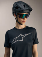 Jersey Stella A-Dura Ride de mujer en negro, logo gris en el pecho, casco de MTB y gafas de sol de ciclismo.