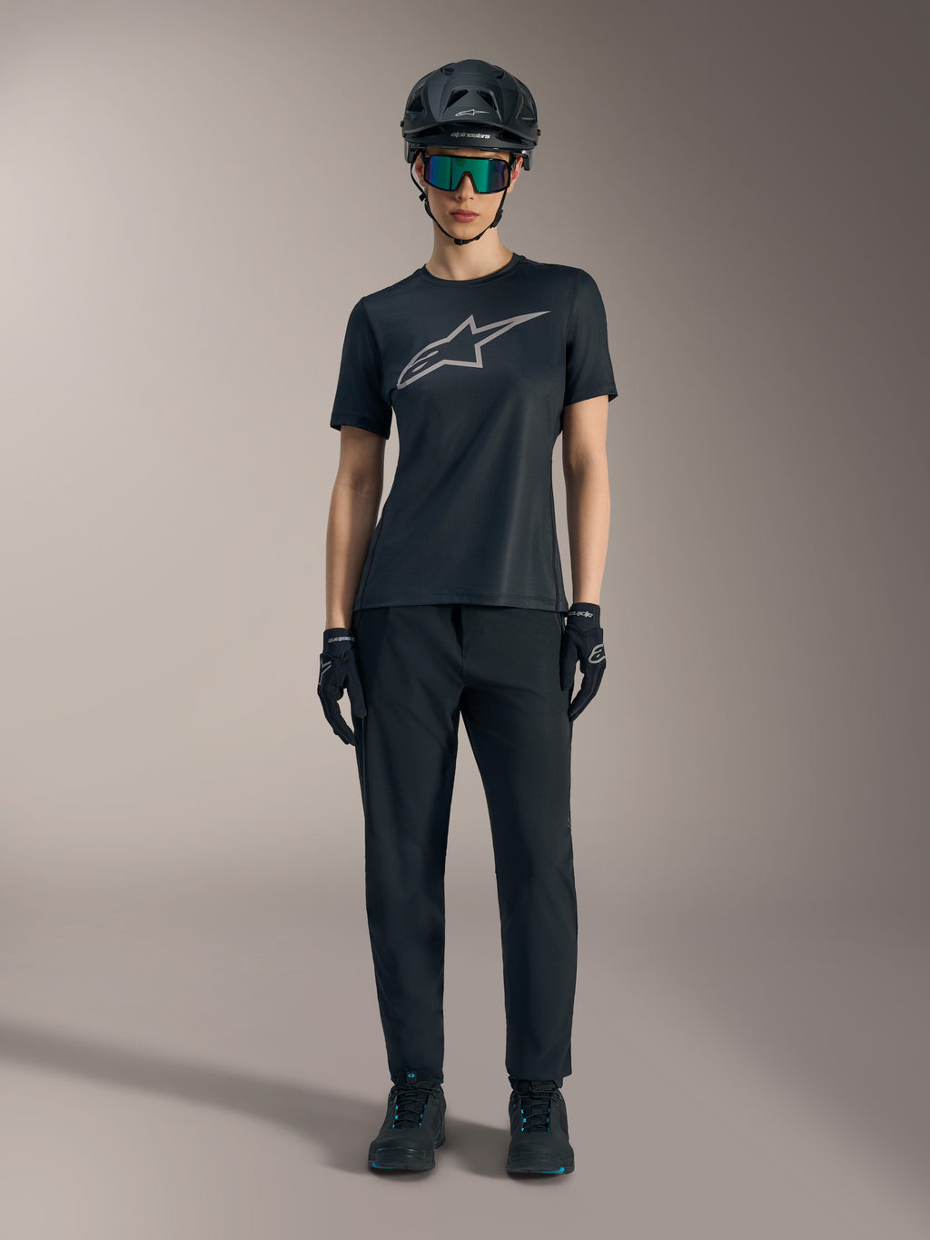 Camiseta Stella A-Dura Ride para mujer, negra con logo plateado, combinada con pantalones de MTB y casco.