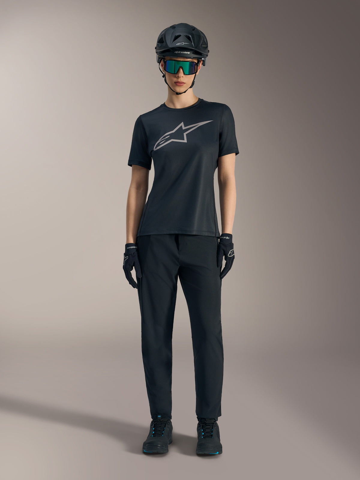 Camiseta Stella A-Dura Ride para mujer, negra con logo plateado, combinada con pantalones de MTB y casco.