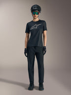 Camiseta Stella A-Dura Ride para mujer, negra con logo plateado, combinada con pantalones de MTB y casco.