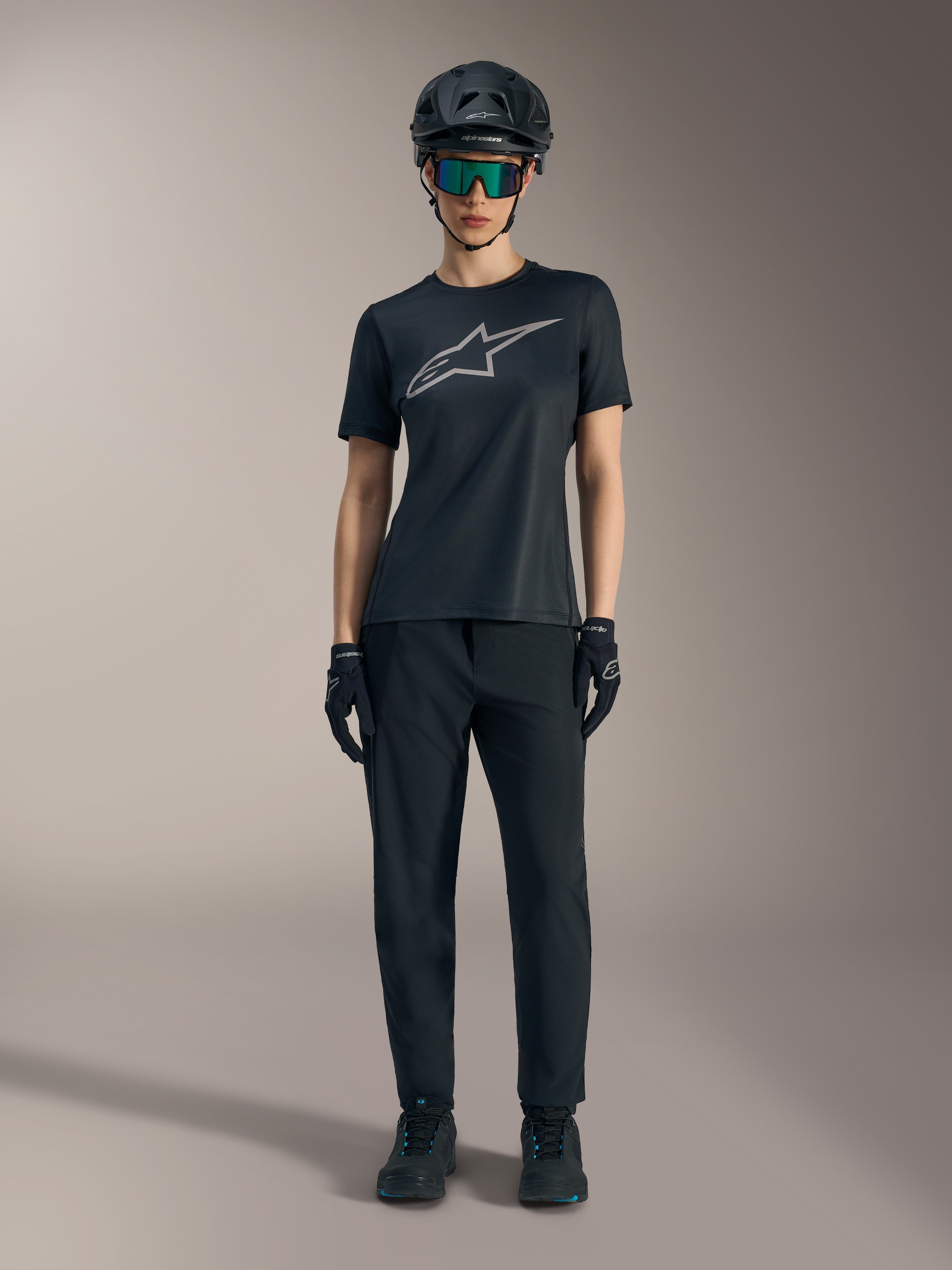 Camiseta Stella A-Dura Ride para mujer, negra con logo plateado, combinada con pantalones de MTB y casco.