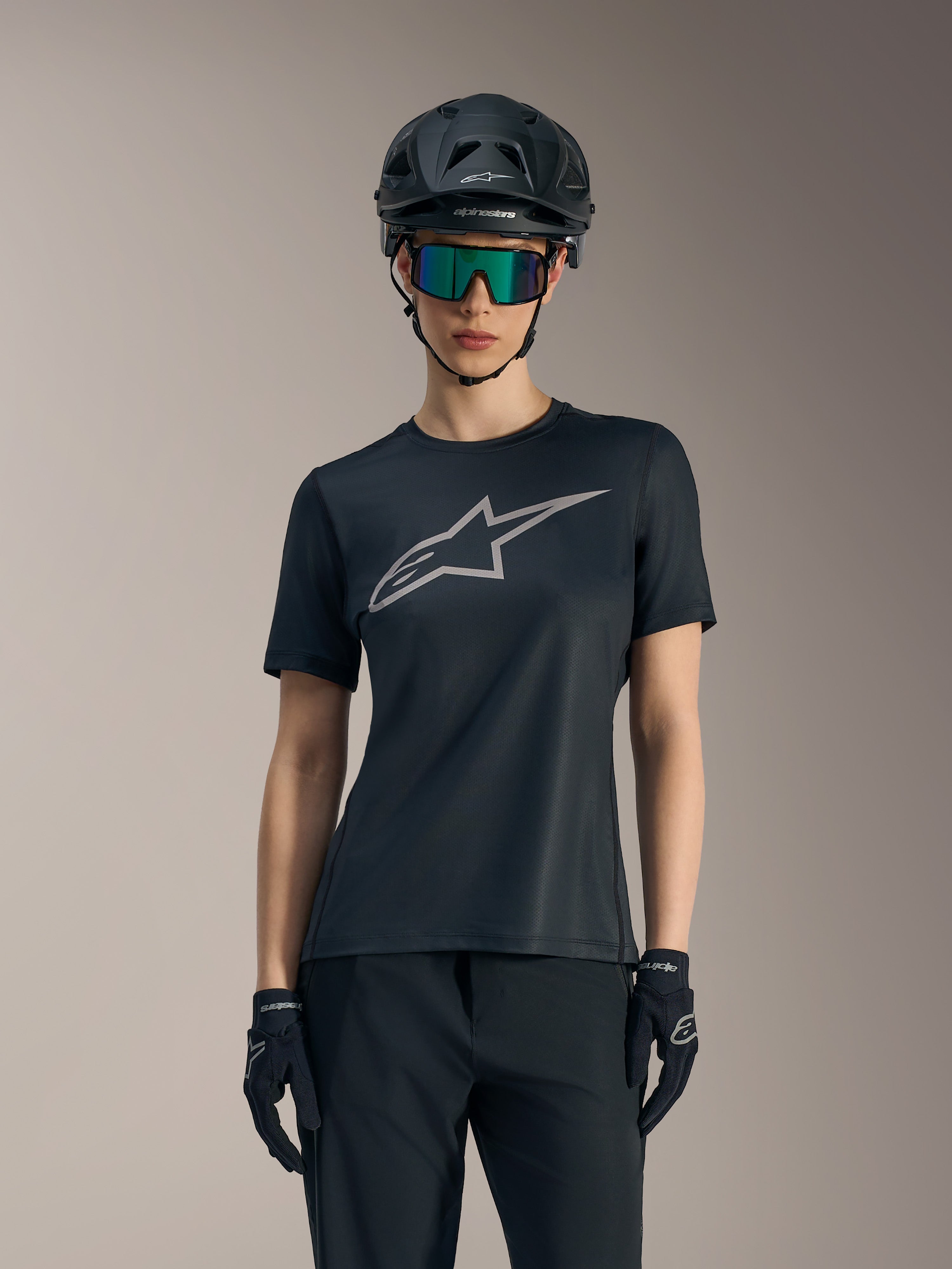Jersey Alpinestars Stella A-Dura Ride negra de mujer, logotipo gris, casco de MTB y gafas técnicas.
