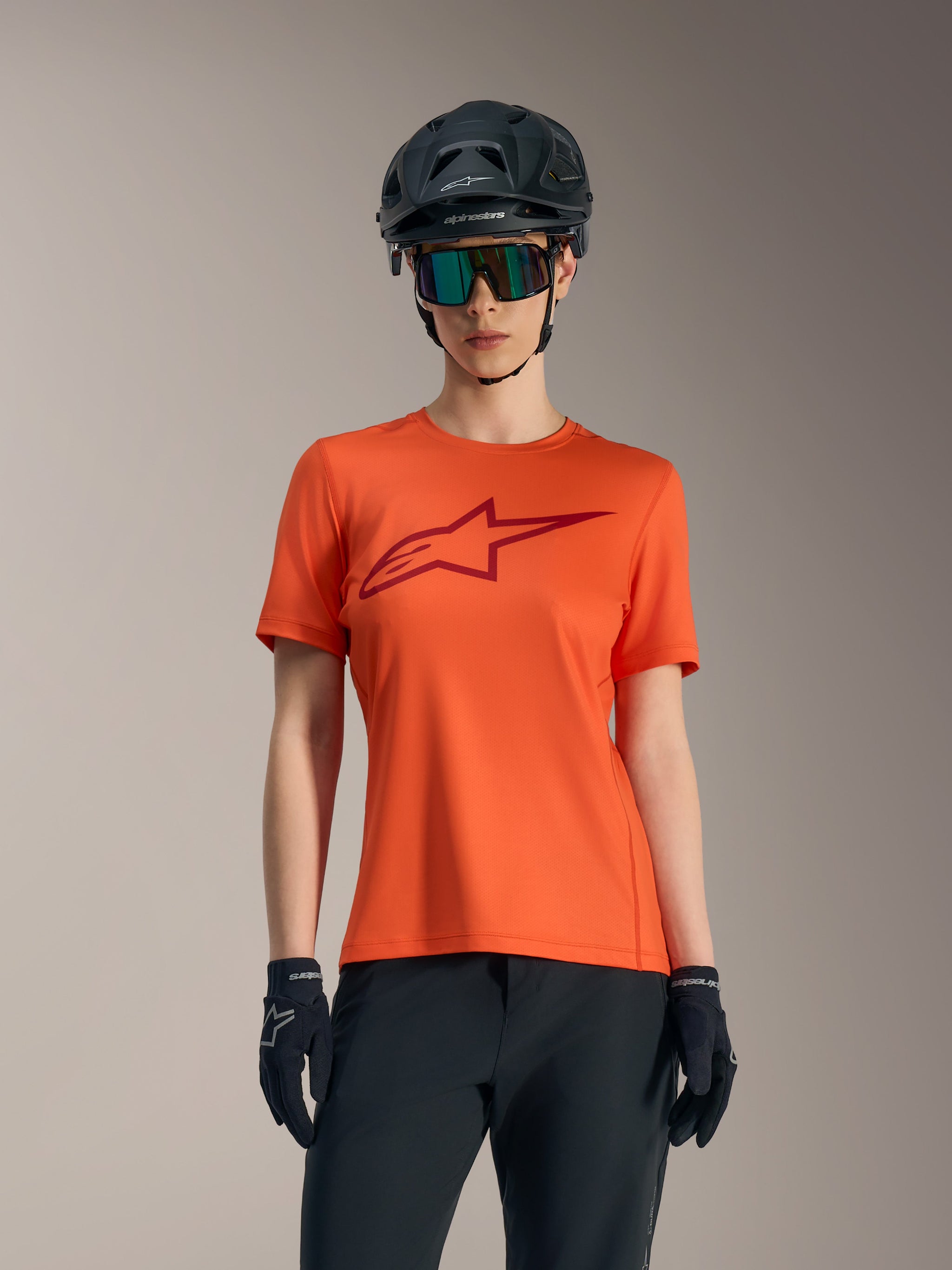 Jersey Alpinestars Stella A-Dura Ride naranja para mujer, logo rojo, casco de MTB negro y gafas de sol.