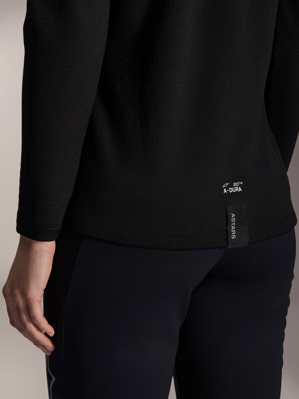 Alpinestars Stella A-Dura Thermal Jersey para mujer, jersey térmico de MTB negro, primer plano del dobladillo inferior trasero con marca A-DURA blanca y etiqueta vertical con el logotipo ASTARS, diseñado para ciclismo de montaña en climas fríos