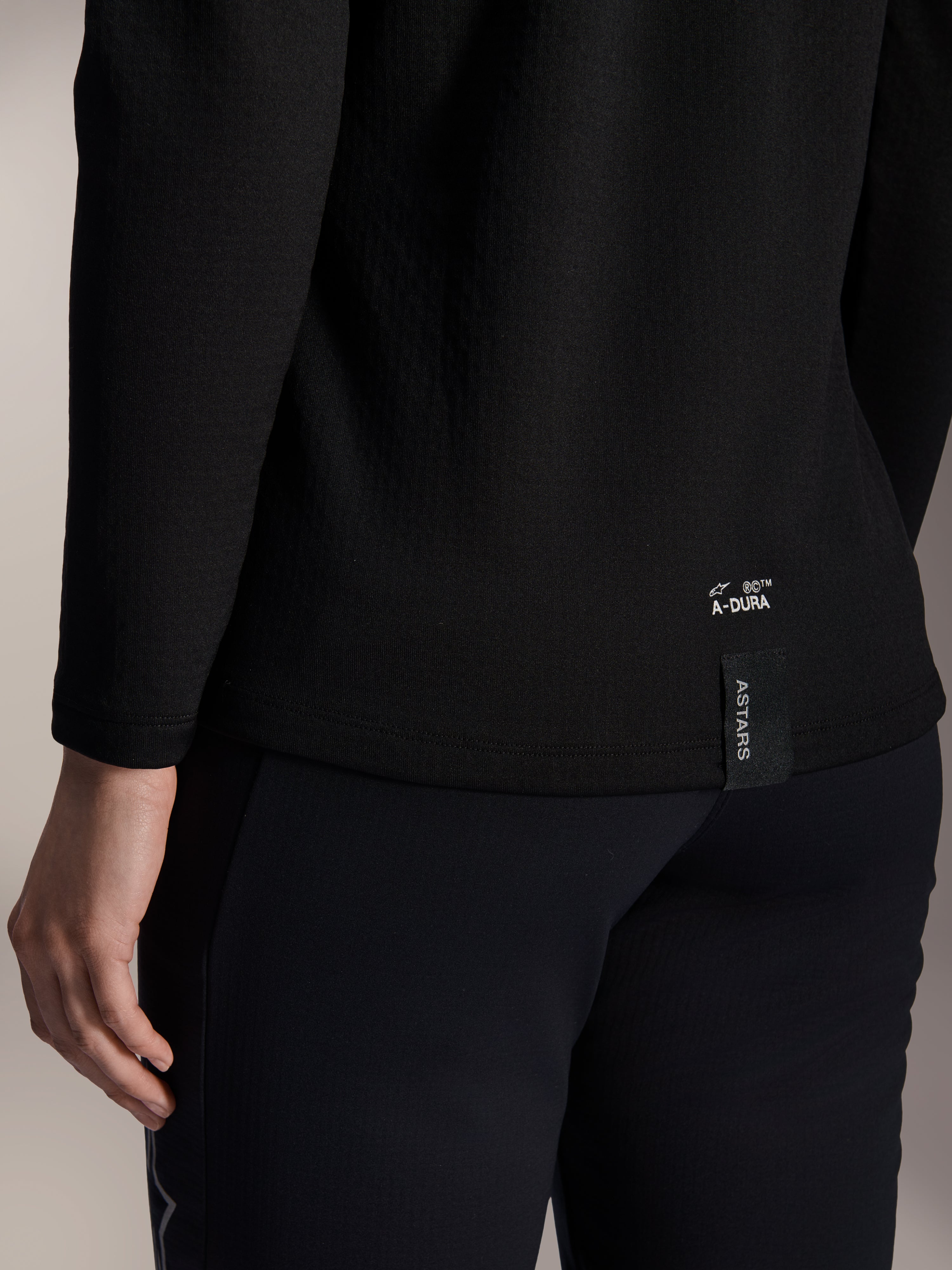 Alpinestars Stella A-Dura Thermal Jersey para mujer, jersey térmico de MTB negro, primer plano del dobladillo inferior trasero con marca A-DURA blanca y etiqueta vertical con el logotipo ASTARS, diseñado para ciclismo de montaña en climas fríos