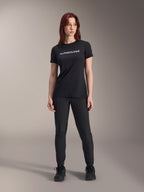 Modelo luciendo el jersey de manga corta Alpinestars Stella A-Dura Dri Switch para mujer en color negro, con logotipo blanco en el pecho, combinado con pantalones técnicos negros y calzado deportivo negro, fotografía de estudio de cuerpo completo