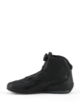 Zapatillas Alpinestars Celer, zapatillas de conducción deportiva y de competición, negro y gris oscuro, vista de perfil lateral con el dial del sistema de cierre Rotor integrado, construcción de microfibra técnica con marca Alpinestars, diseño aerodinámico para alto rendimiento