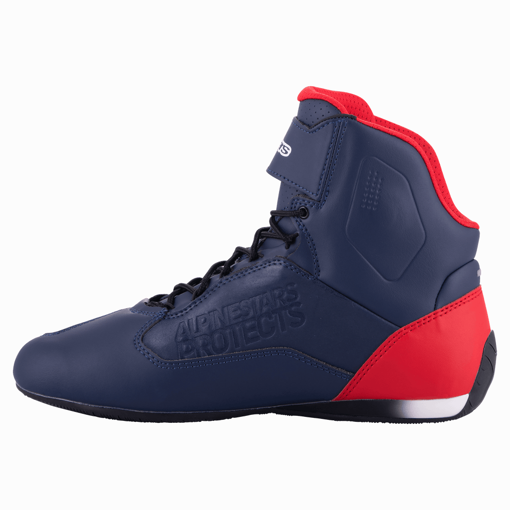 Zapatilla de moto Alpinestars Austin, azul marino y rojo brillante, vista de perfil que muestra la parte superior de microfibra con detalles en rojo en el talón y el cuello, cordones negros, marca grabada 'Alpinestars Protects', calzado de motociclismo de caña alta