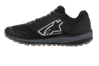 Alpinestars Meta Trail Shoes, calzado de running de alto rendimiento, negro y gris oscuro, perfil lateral con gran logotipo Astars blanco, entresuela gris oscuro, suela de goma con tacos resistente al aceite, diseñado para comodidad en el paddock y uso por equipos de automovilismo