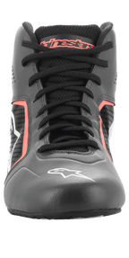 Zapatos Alpinestars Tech-1 K Start V2, zapatillas de karting, color negro asfalto y naranja flúor, vista frontal que muestra cordones negros, marca Alpinestars naranja en la lengüeta, logotipo de estrella blanca en la puntera y paneles de microfibra perforada