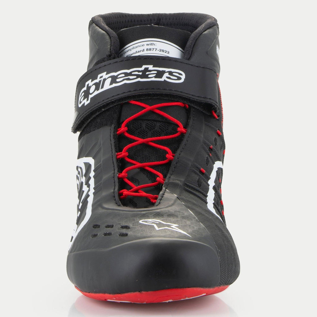 Zapatos Alpinestars Tech-1 KX V3, zapatos de karting, negros, blancos y rojos, vista frontal que presenta cordones asimétricos rojos, una correa de velcro negra en el tobillo con el logo en blanco y una etiqueta de certificación FIA 8877-2022 visible en la lengüeta.