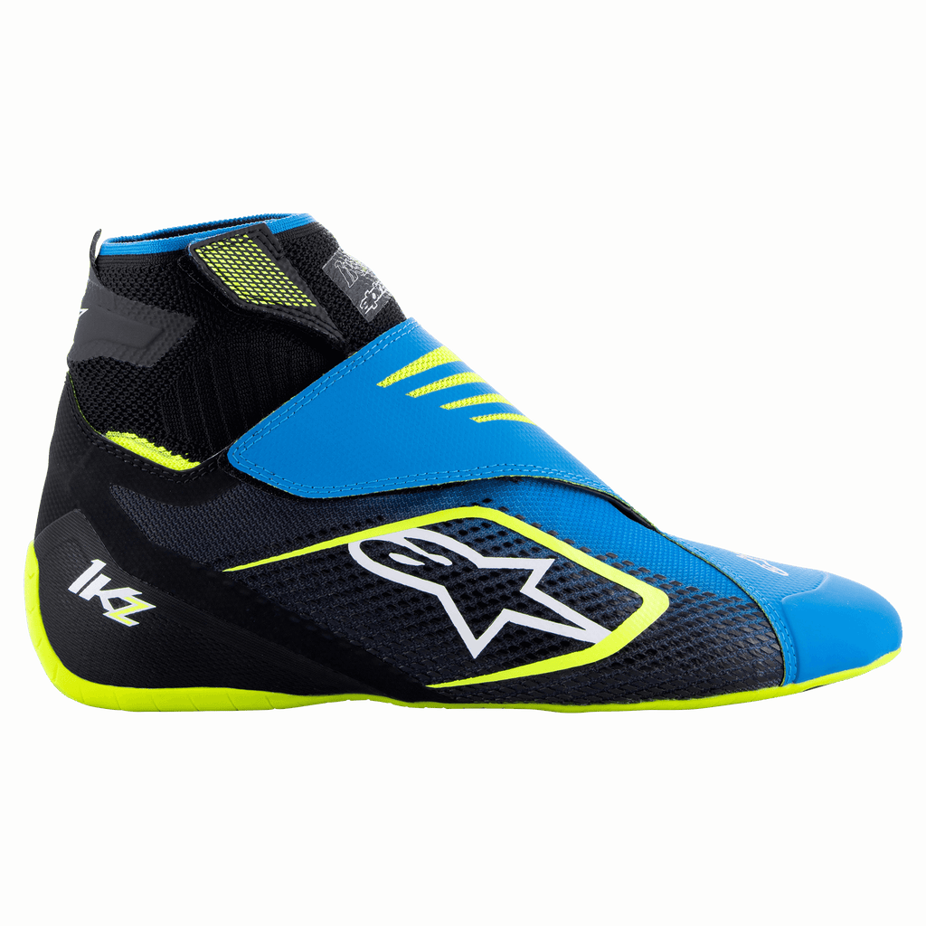 Alpinestars Tech-1 KZ V2, zapatos de karting, negro, azul esmaltado y amarillo fluorescente, vista lateral que muestra la parte superior de punto, cierre de doble correa y el prominente logotipo blanco de Alpinestars, diseñados para la sensibilidad con los pedales en el automovilismo