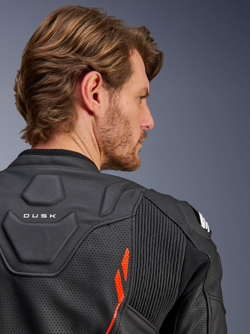 Chaqueta de cuero Alpinestars Dusk Airflow, Negro Rojo Fluo, primer plano de la parte superior de la espalda y el hombro, con cuero perforado para ventilación y paneles elásticos en acordeón, detalle de la marca 'DUSK', usada por un modelo masculino