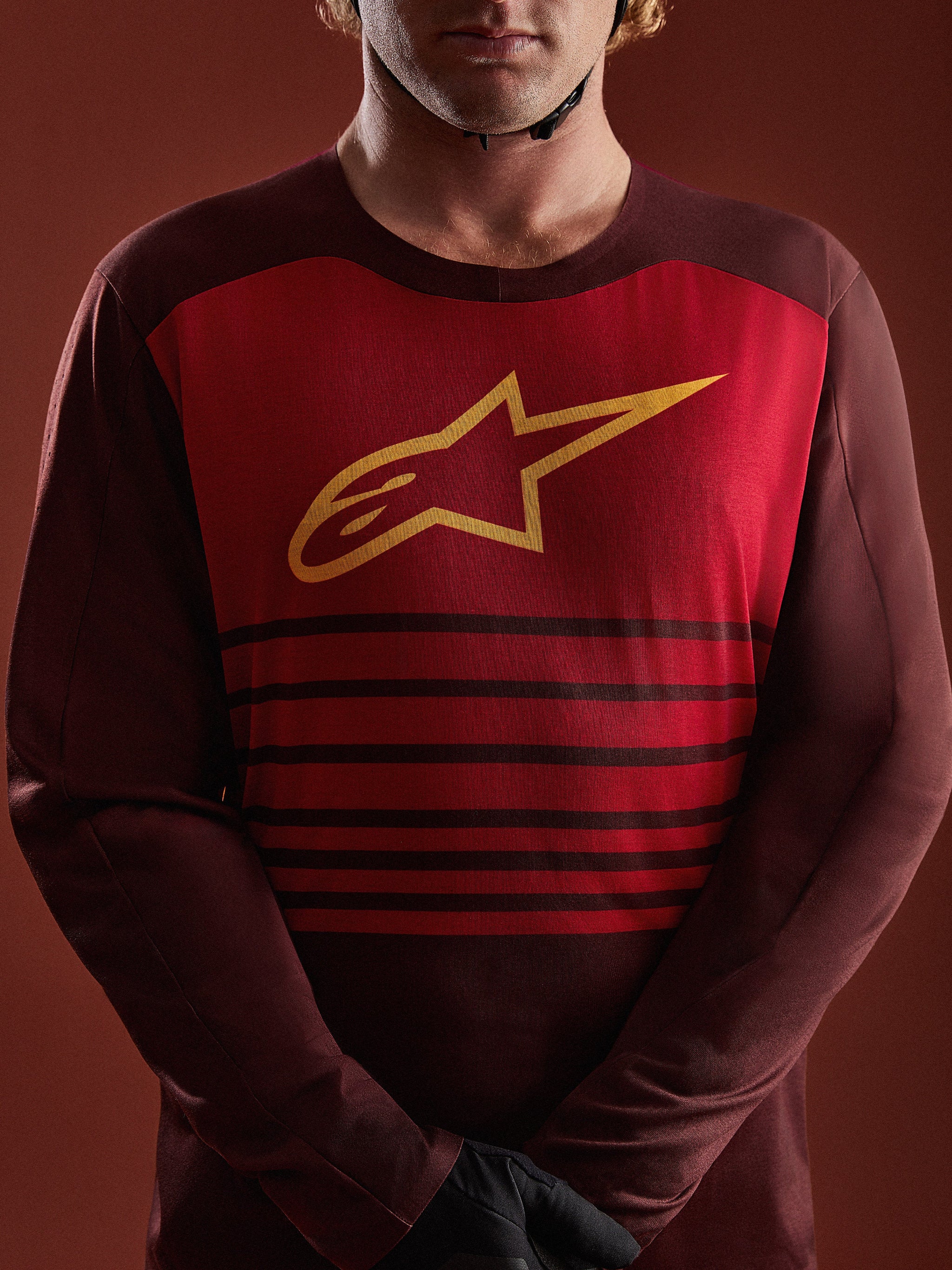 Jersey A-Dura Elite de Alpinestars burdeos, con panel frontal rojo, logo A-star amarillo y franjas horizontales.