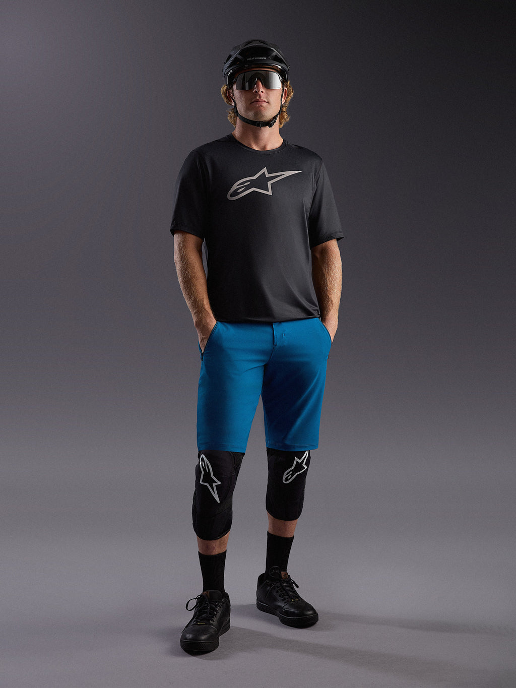 Jersey Alpinestars A-Dura Ride SS negro y shorts azules, equipo de MTB completo con rodilleras y casco.