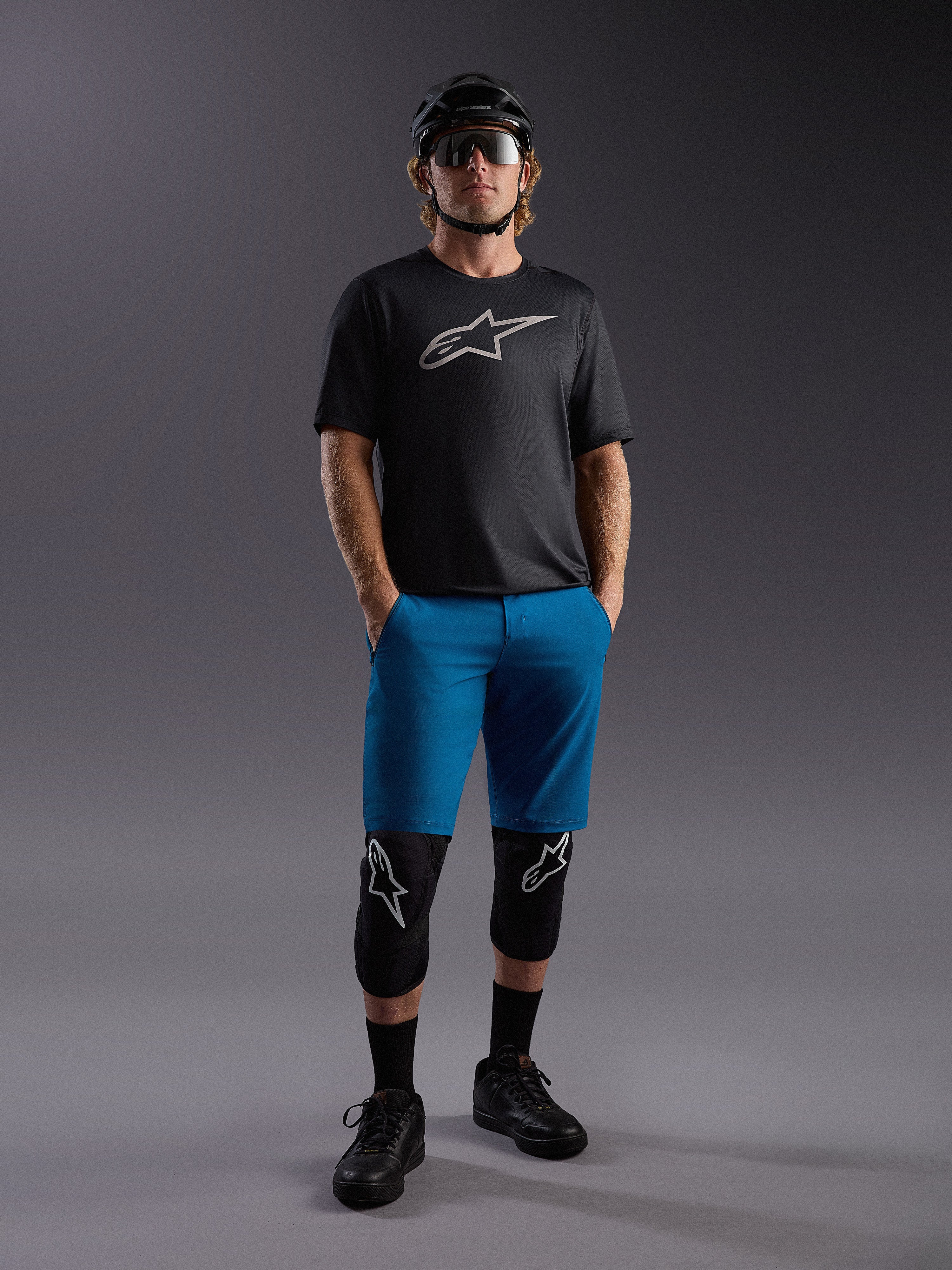 Jersey Alpinestars A-Dura Ride SS negro y shorts azules, equipo de MTB completo con rodilleras y casco.