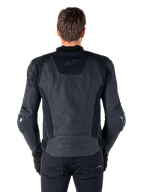 Vista trasera de un piloto con la chaqueta de cuero Alpinestars Missile V3 en color negro, destacando su construcción en cuero premium con paneles elásticos técnicos, logotipo de Alpinestars en relieve en la parte inferior de la espalda y marca sutil en la parte superior, combinada con pantalones negros para un look deportivo de competición.