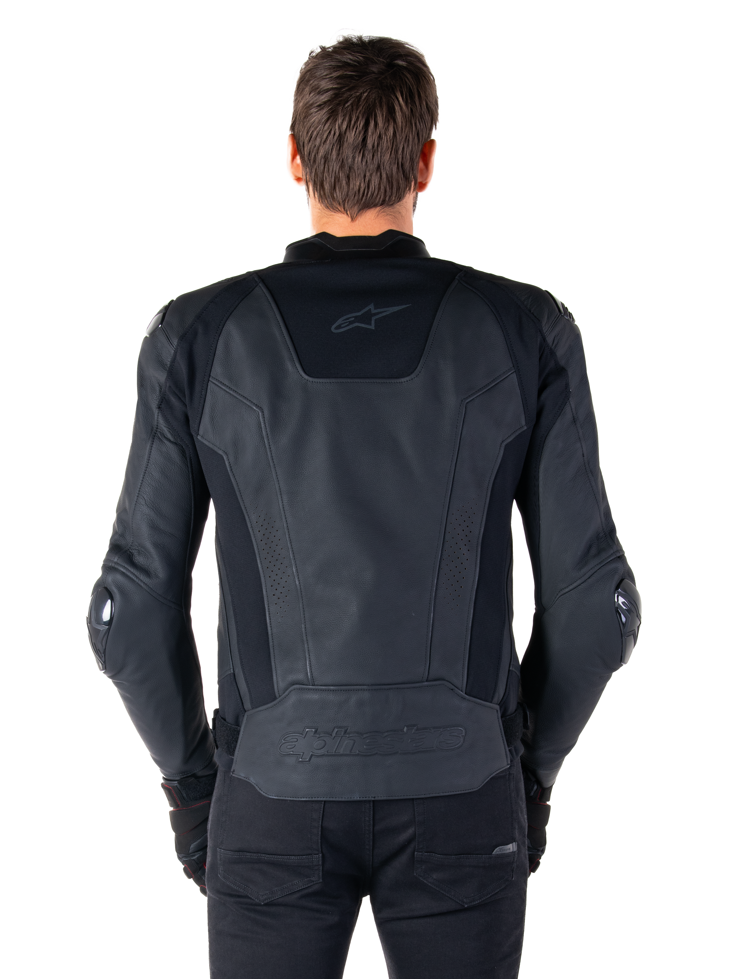 Vista trasera de un piloto con la chaqueta de cuero Alpinestars Missile V3 en color negro, destacando su construcción en cuero premium con paneles elásticos técnicos, logotipo de Alpinestars en relieve en la parte inferior de la espalda y marca sutil en la parte superior, combinada con pantalones negros para un look deportivo de competición.