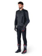 Chaqueta de cuero Alpinestars Missile V3, negra, usada por un piloto con pantalones negros y guantes y botas de carreras en negro y rojo, con paneles de cuero perforado y logotipos monocromáticos elegantes, estética deportiva de competición profesional