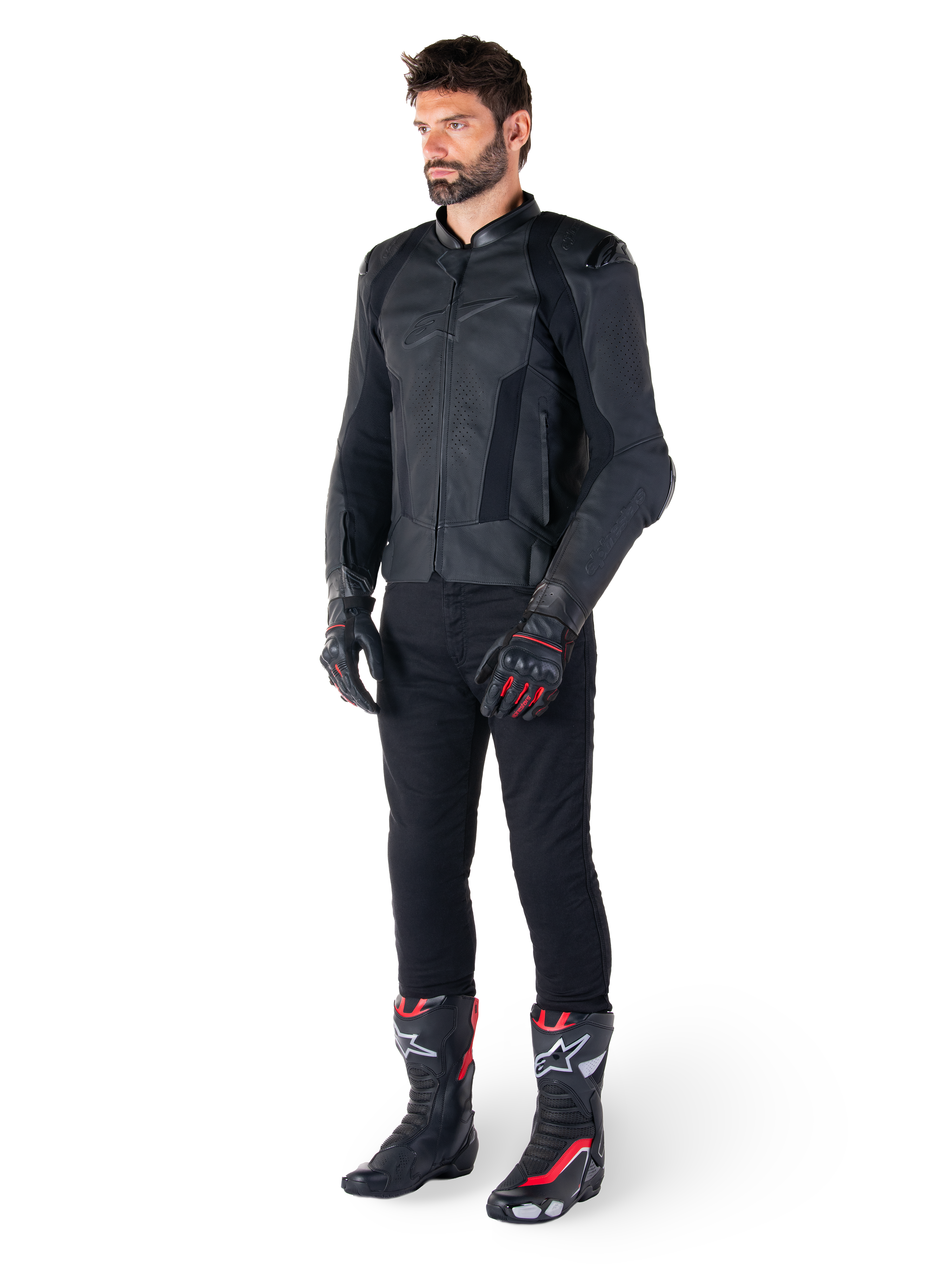 Chaqueta de cuero Alpinestars Missile V3, negra, usada por un piloto con pantalones negros y guantes y botas de carreras en negro y rojo, con paneles de cuero perforado y logotipos monocromáticos elegantes, estética deportiva de competición profesional
