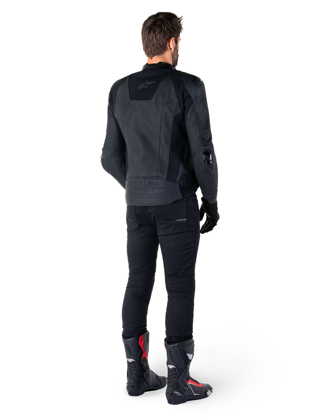 Chaqueta de cuero Alpinestars Missile V3 en color negro, vista trasera en un piloto, combinada con pantalones negros y botas de competición negras y rojas, con una elegante confección en cuero, logotipos en el mismo tono y un ajuste de alto rendimiento para competición