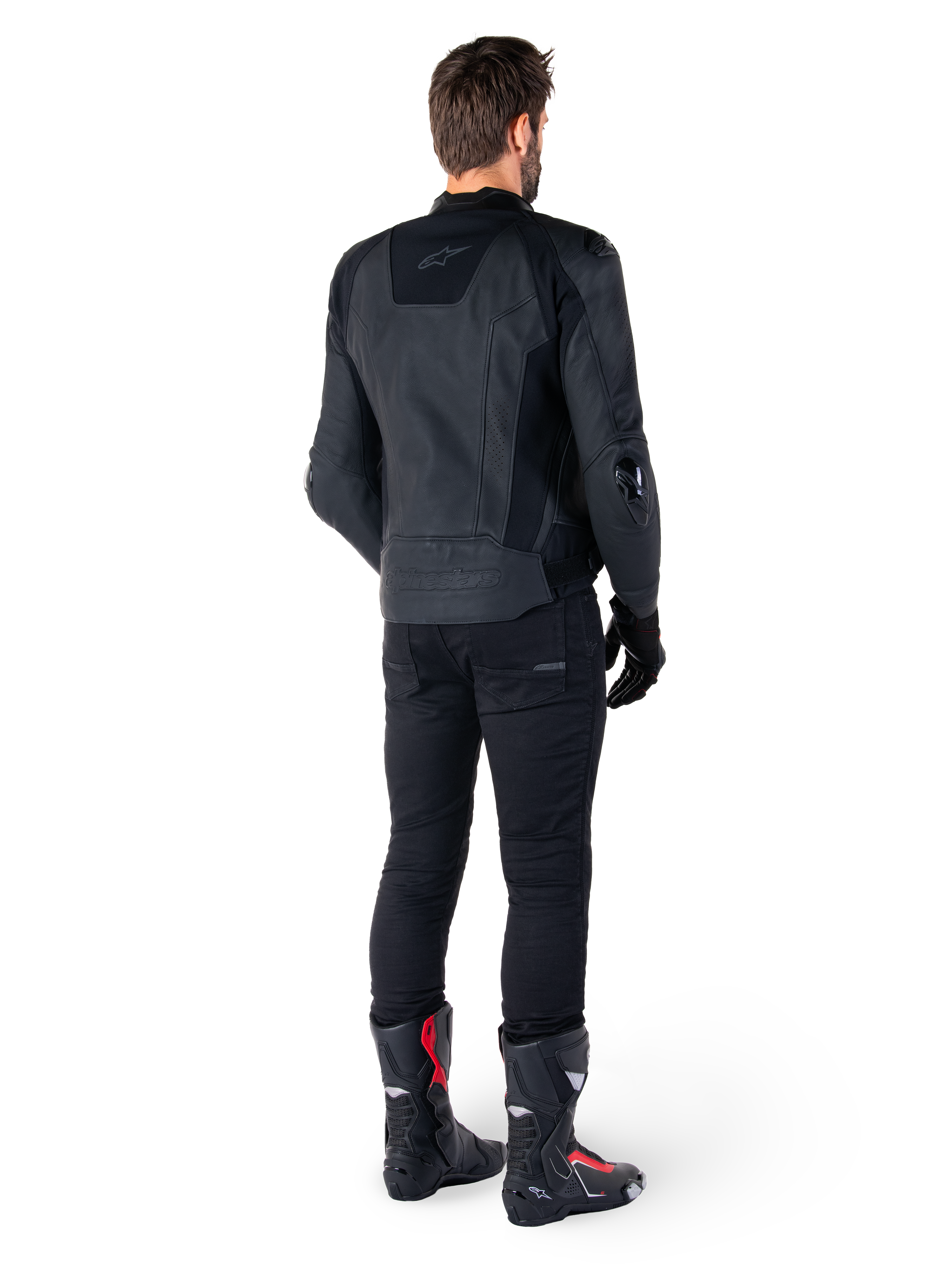 Chaqueta de cuero Alpinestars Missile V3 en color negro, vista trasera en un piloto, combinada con pantalones negros y botas de competición negras y rojas, con una elegante confección en cuero, logotipos en el mismo tono y un ajuste de alto rendimiento para competición