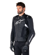 Chaqueta de cuero Alpinestars Missile V3, en color negro y blanco, usada por un hombre con guantes de moto negros, con un logotipo de Alpinestars blanco prominente en el pecho, deslizadores externos en los hombros y paneles perforados para un estilo inspirado en las carreras.