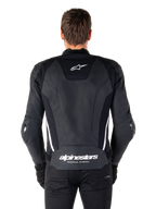 Vista posterior de la chaqueta de cuero Alpinestars Missile V3 en negro y blanco, con el logotipo de la estrella de Alpinestars en la parte superior de la espalda y la marca en la zona lumbar inferior, franjas verticales blancas y deslizadores externos en los codos, chaqueta deportiva de carreras de cuero premium.
