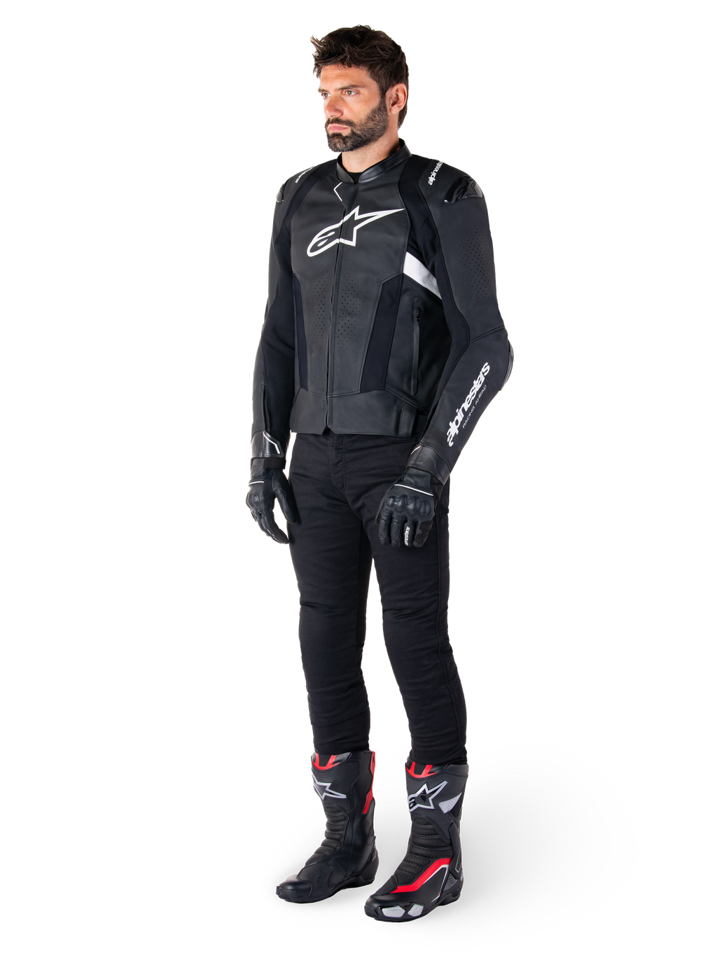 Piloto masculino con la chaqueta de cuero Alpinestars Missile V3 en negro y blanco, con un logotipo blanco en el pecho y paneles de cuero perforado, combinada con pantalones de montar negros, guantes negros y botas de carreras negras y rojas para un look deportivo completo.