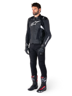 Piloto masculino con la chaqueta de cuero Alpinestars Missile V3 en negro y blanco, con un logotipo blanco en el pecho y paneles de cuero perforado, combinada con pantalones de montar negros, guantes negros y botas de carreras negras y rojas para un look deportivo completo.
