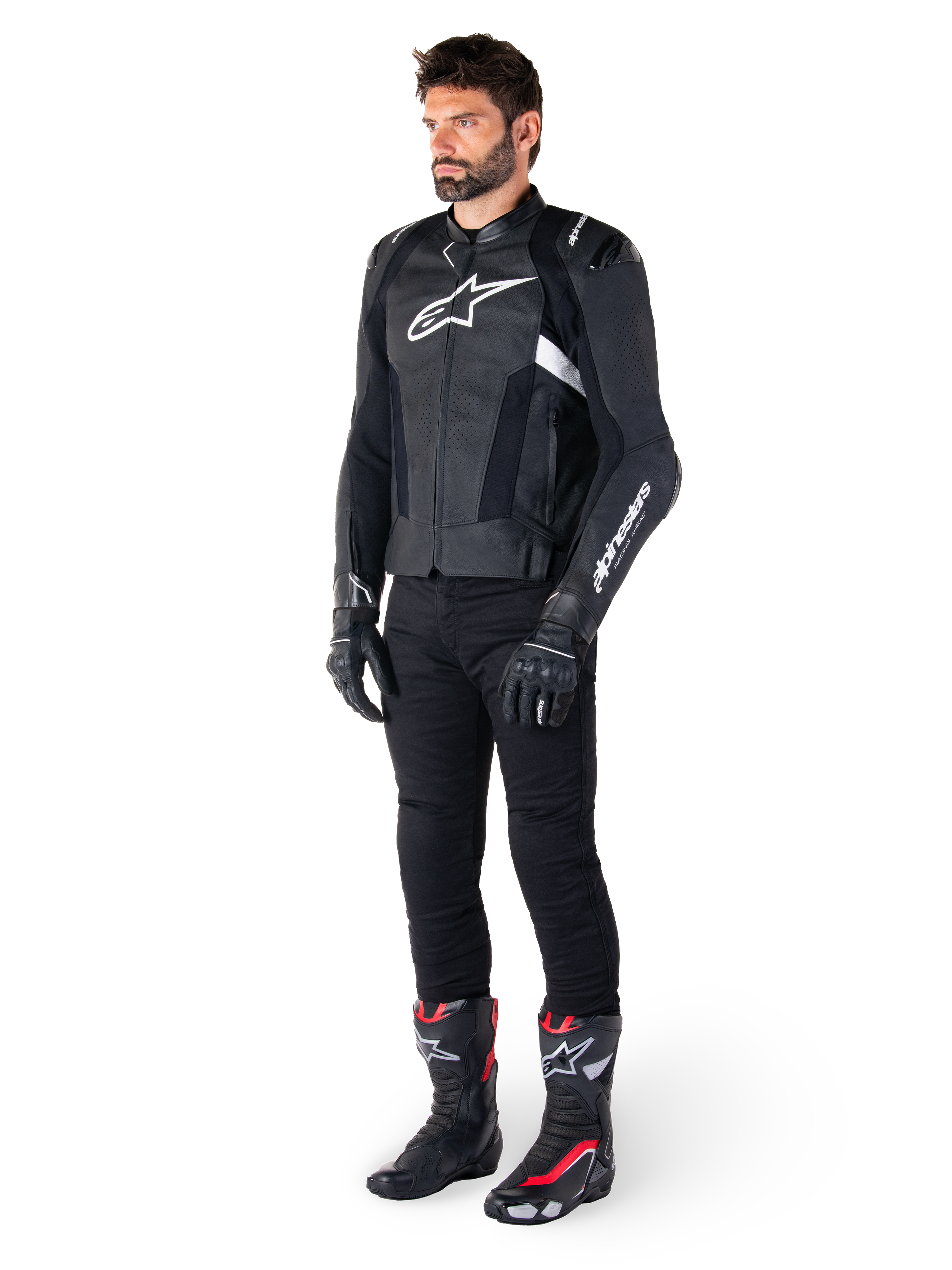 Piloto masculino con la chaqueta de cuero Alpinestars Missile V3 en negro y blanco, con un logotipo blanco en el pecho y paneles de cuero perforado, combinada con pantalones de montar negros, guantes negros y botas de carreras negras y rojas para un look deportivo completo.