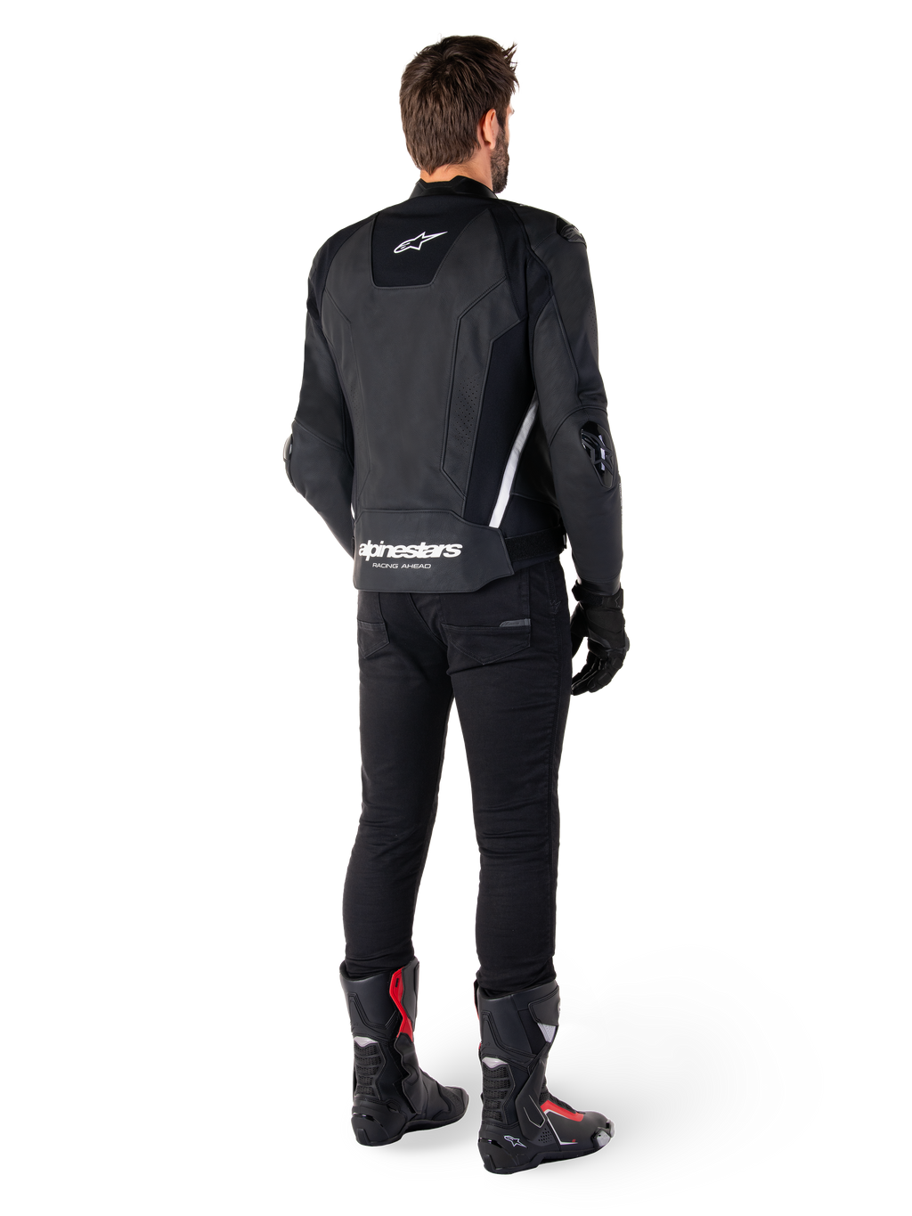 Chaqueta de cuero Alpinestars Missile V3, negra y blanca, vista trasera sobre el piloto, con la marca Alpinestars en blanco llamativo en la parte inferior de la espalda y un logotipo pequeño en la parte superior de la espalda, usada con pantalones negros y botas de carreras, confección en cuero premium para competición de motociclismo.