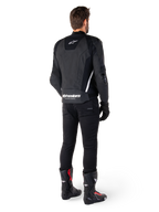 Chaqueta de cuero Alpinestars Missile V3, negra y blanca, vista trasera sobre el piloto, con la marca Alpinestars en blanco llamativo en la parte inferior de la espalda y un logotipo pequeño en la parte superior de la espalda, usada con pantalones negros y botas de carreras, confección en cuero premium para competición de motociclismo.