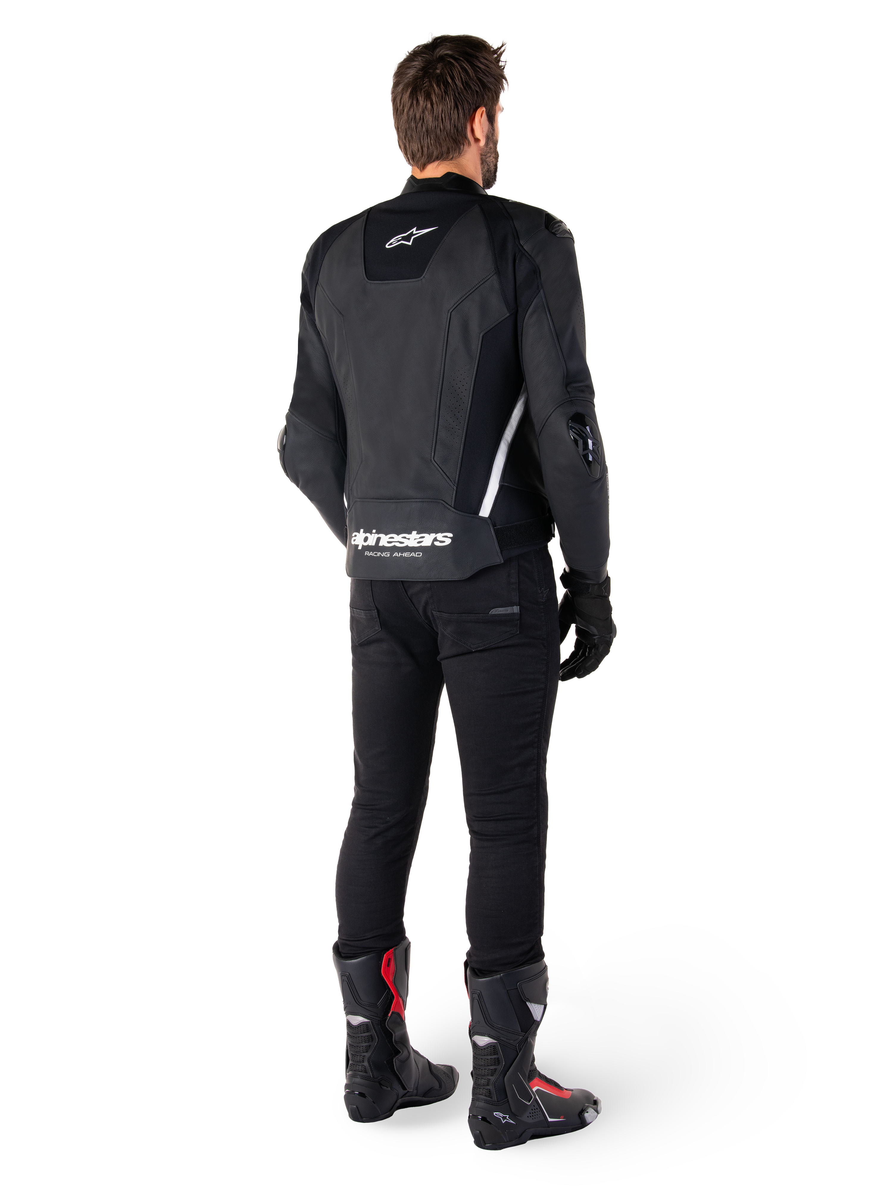 Chaqueta de cuero Alpinestars Missile V3, negra y blanca, vista trasera sobre el piloto, con la marca Alpinestars en blanco llamativo en la parte inferior de la espalda y un logotipo pequeño en la parte superior de la espalda, usada con pantalones negros y botas de carreras, confección en cuero premium para competición de motociclismo.