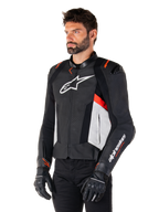 Chaqueta de cuero Alpinestars Missile V3, negro, blanco y rojo flúor, chaqueta de moto deportiva de competición usada por un modelo con guantes y pantalones negros, con paneles de cuero perforado y logotipos de Alpinestars destacados