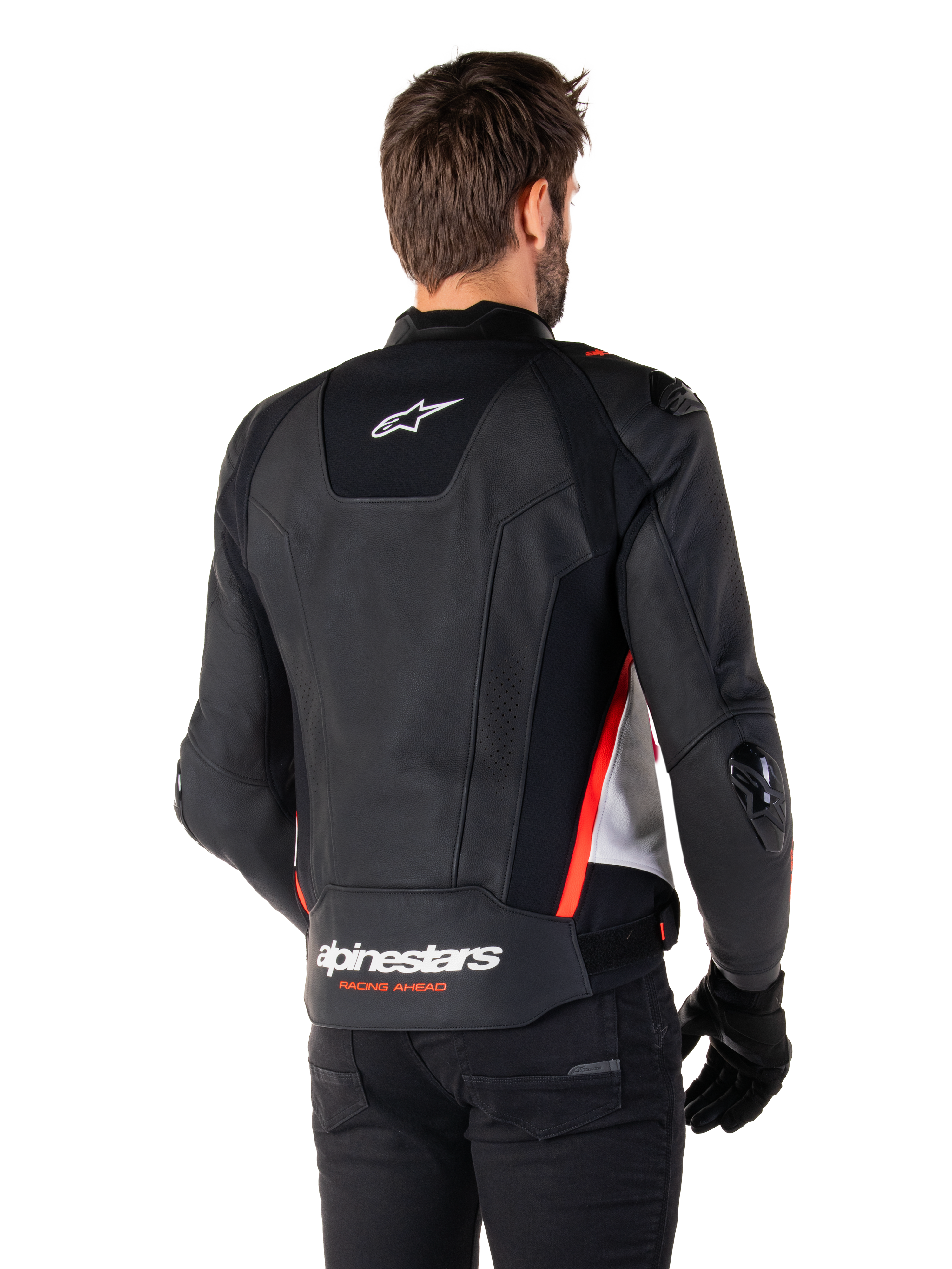 Chaqueta de cuero Alpinestars Missile V3, vista posterior en un piloto, Negro, Blanco y Rojo Flúor, con el distintivo logotipo de Alpinestars y el texto 'RACING AHEAD' en la parte inferior de la espalda, confección en cuero premium con paneles elásticos técnicos y deslizadores protectores de TPU, usada con guantes y pantalones negros.